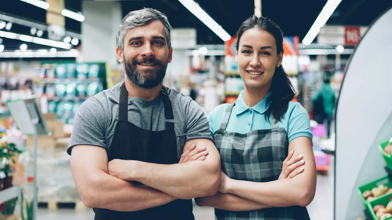 Two smiling shop employees in aprons - staff attendance, leave and salary management for retail